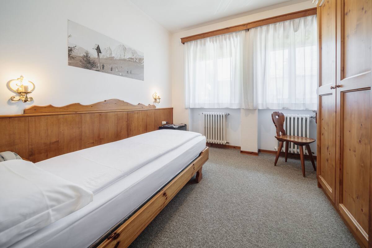 A bedroom with a wooden bed, a nightstand, a chair, a radiator, and a window with curtains.
