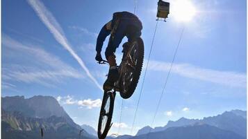 Un ciclista de montaña en pleno salto, con un teleférico al fondo.