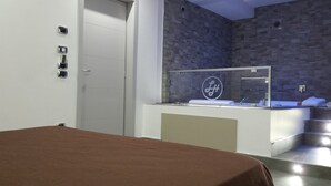 Quarto de hotel moderno com cama, banheiro com box de vidro e parede texturizada.