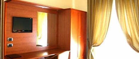 Una habitación de hotel con un escritorio de madera, un televisor en la pared y un ventanal con cortinas.