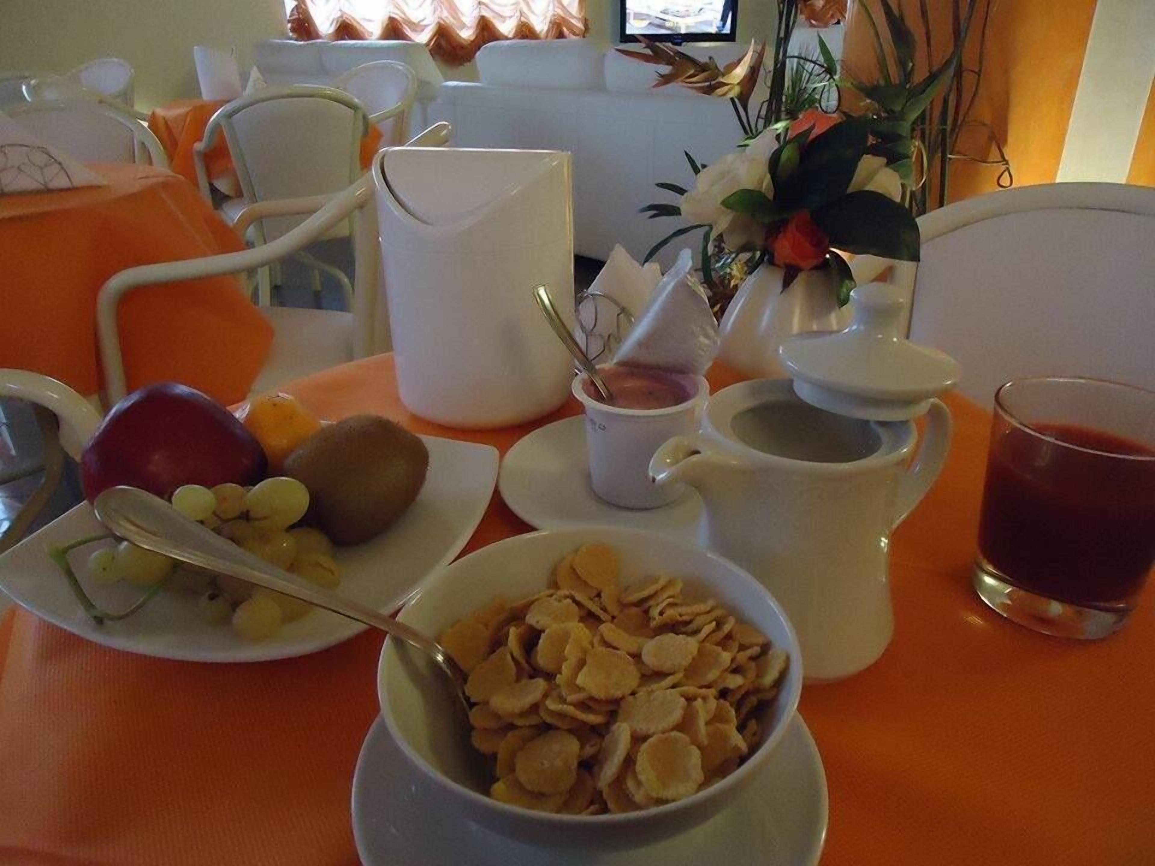 Ein Frühstückstisch mit Schüssel für Müsli, Obstteller, Milchkrug, Glas Saft und Blumen.