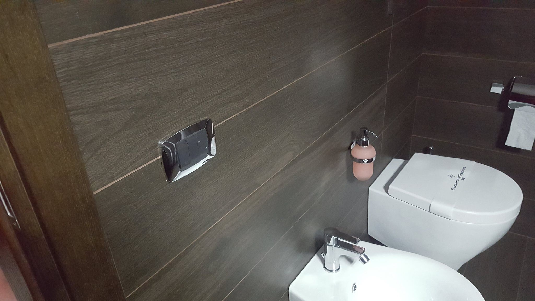 A modern bathroom with a white toilet, a sink, and a soap dispenser on the wall.
