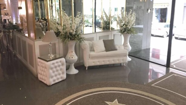 Um hall moderno com um sofá branco, uma mesinha e dois vasos grandes com flores brancas.