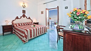 A bedroom with a bed, a desk, a chair, a vase of flowers, and a balcony door. - La Rosa dei Venti (Positano)