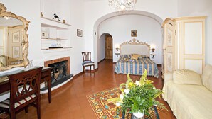 A room with a fireplace, a bed with a patterned bedspread, a sofa, a wooden chair, and a large mirror. - La Rosa dei Venti (Positano)
