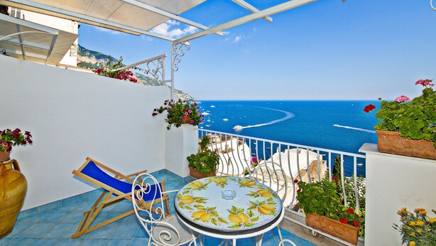 A balcony with a view of the sea, a table with a floral tablecloth, and potted plants. - La Rosa dei Venti (Positano)
