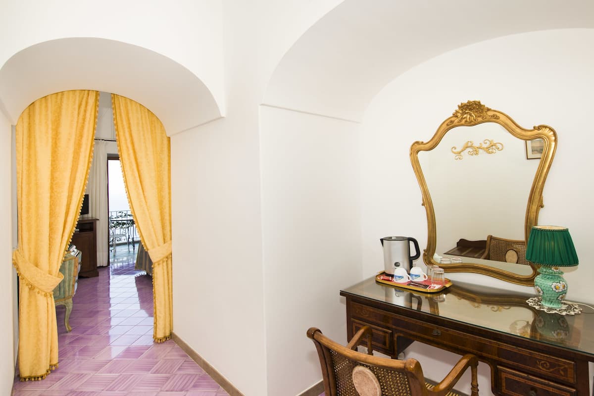 Une pièce comprenant une commode en bois, un miroir avec un cadre orné, une lampe verte et un plateau contenant divers objets posés sur la commode.