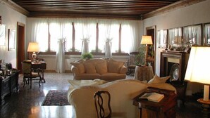 A hotel room with a wooden ceiling, a large bed, a sofa, a chair, a table, and a fireplace. - At Home A Palazzo (Venice)