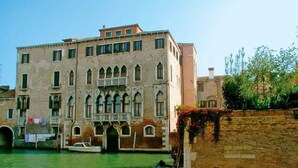 A historic building with multiple windows and balconies, situated by a canal with boats. - At Home A Palazzo (Venice)