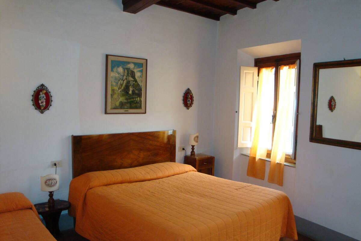 A bedroom with two beds, a wooden headboard, a nightstand with a lamp, a framed picture on the wall, and a window with curtains.