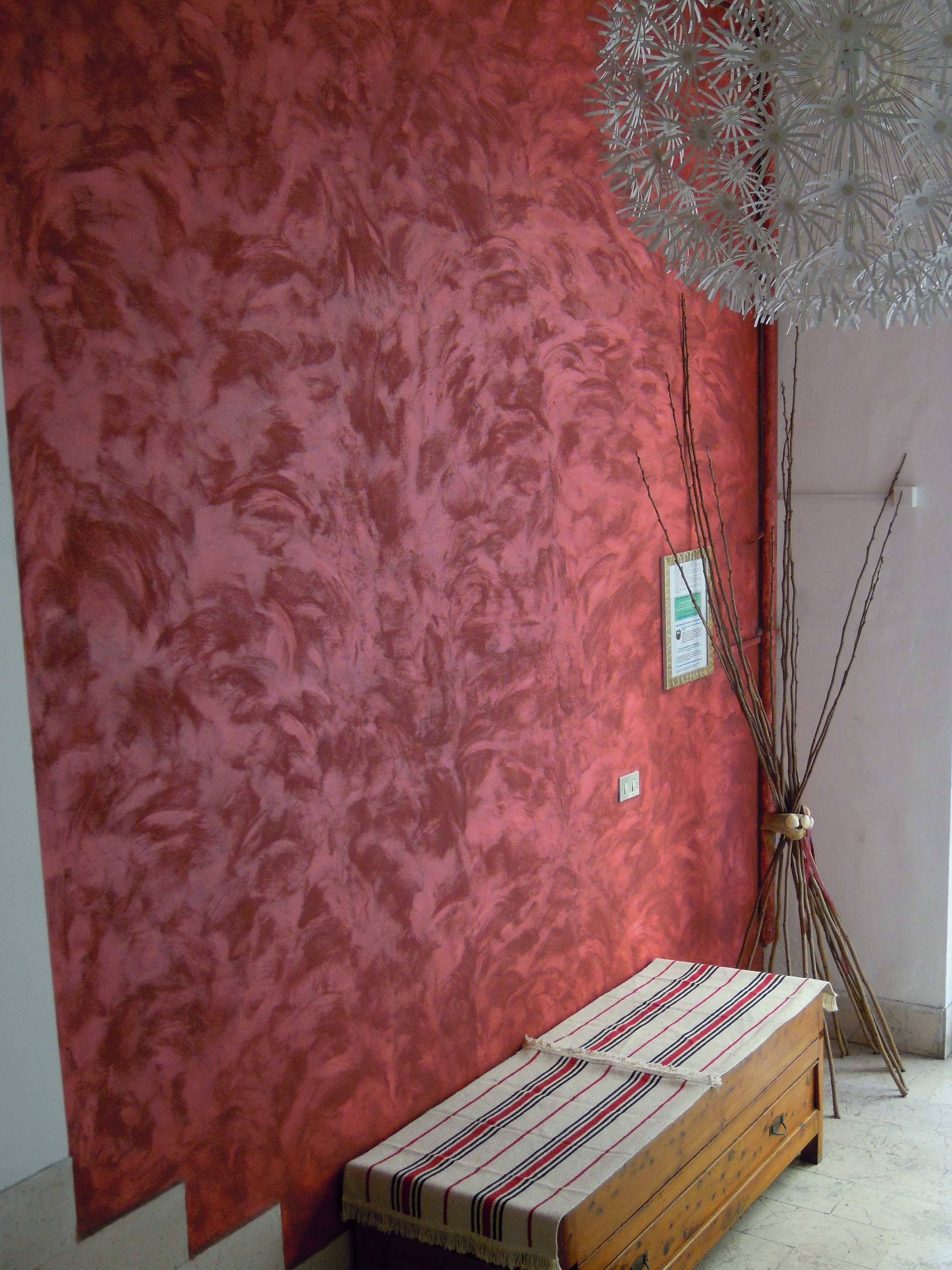 A room with a red textured wall, a wooden bench with a striped cloth, and a decorative white structure.