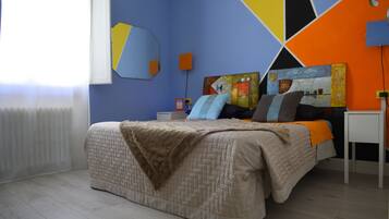 A bedroom with a bed, a bedside table, a wall clock, and a window with blinds.