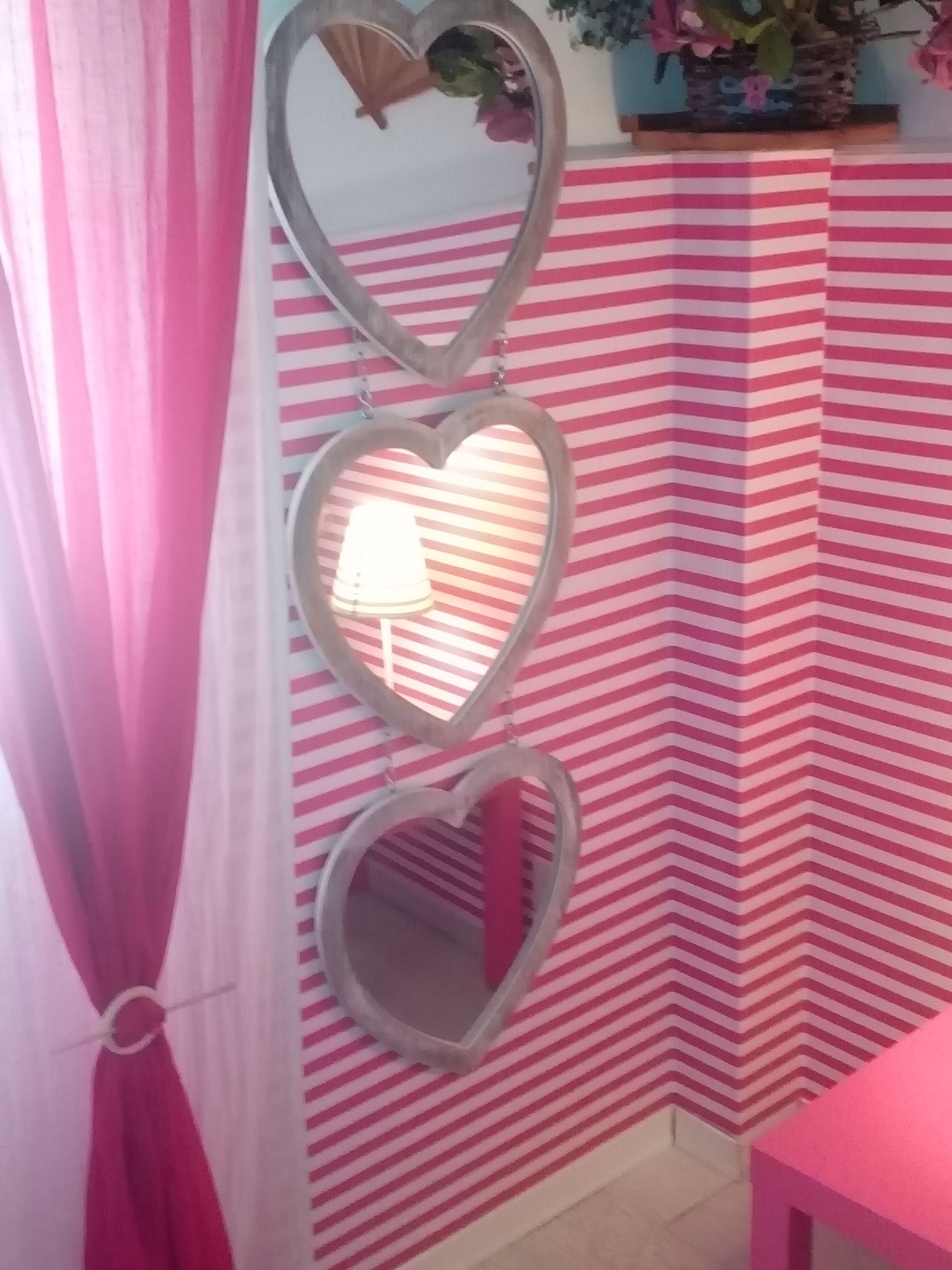 A room with striped wallpaper, a heart-shaped mirror, and a lamp.