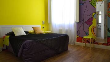 Una habitación con una cama, un taburete pequeño, un espejo y una pared con un mural colorido.