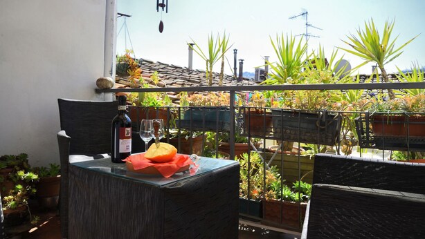 A balcony with a glass table, wicker chairs, and potted plants. - Leonardo's Rooms (Pontassieve)