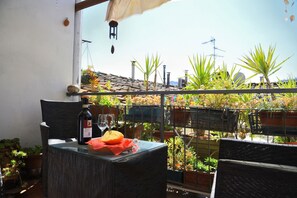 A balcony with a glass table, wicker chairs, and potted plants.