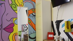 A room with a colorful mural, a mirror, a television, and a desk with a lamp. - Leonardo's Rooms (Pontassieve)