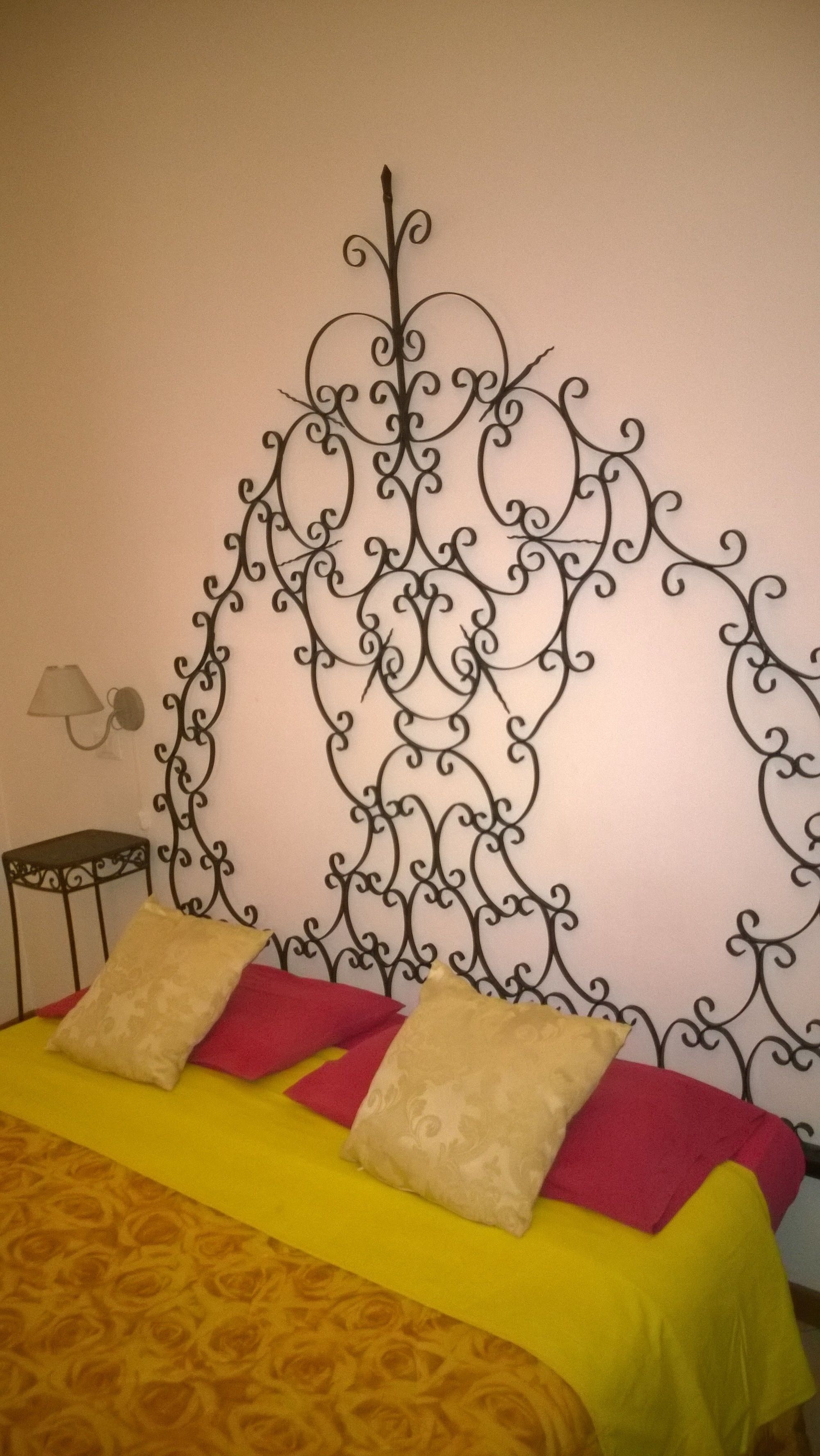 Una cama con cabecera de metal, una lámpara y una colcha estampada.
