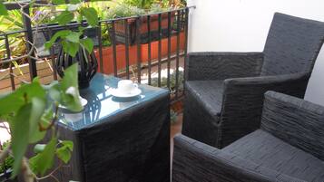 Un balcón con mobiliario de mimbre, una mesa de vidrio y plantas en macetas.