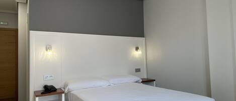 A single-bed room with a white headboard, bedside tables, and wall-mounted lights.