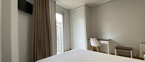 Una habitación de hotel con cama, escritorio, silla, televisión y ventana con cortinas.