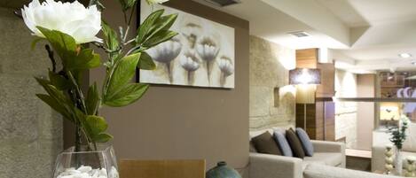A modern interior with a seating area, a large vase with white pebbles, and a wall with a floral painting.