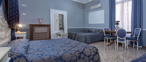 A hotel room with a large bed, a sitting area with a sofa and chairs, a chandelier, and a window with curtains.