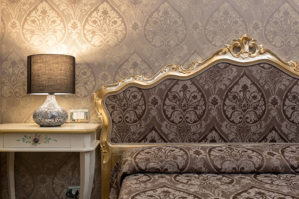 A bed with a patterned headboard and a bedside table with a lamp.