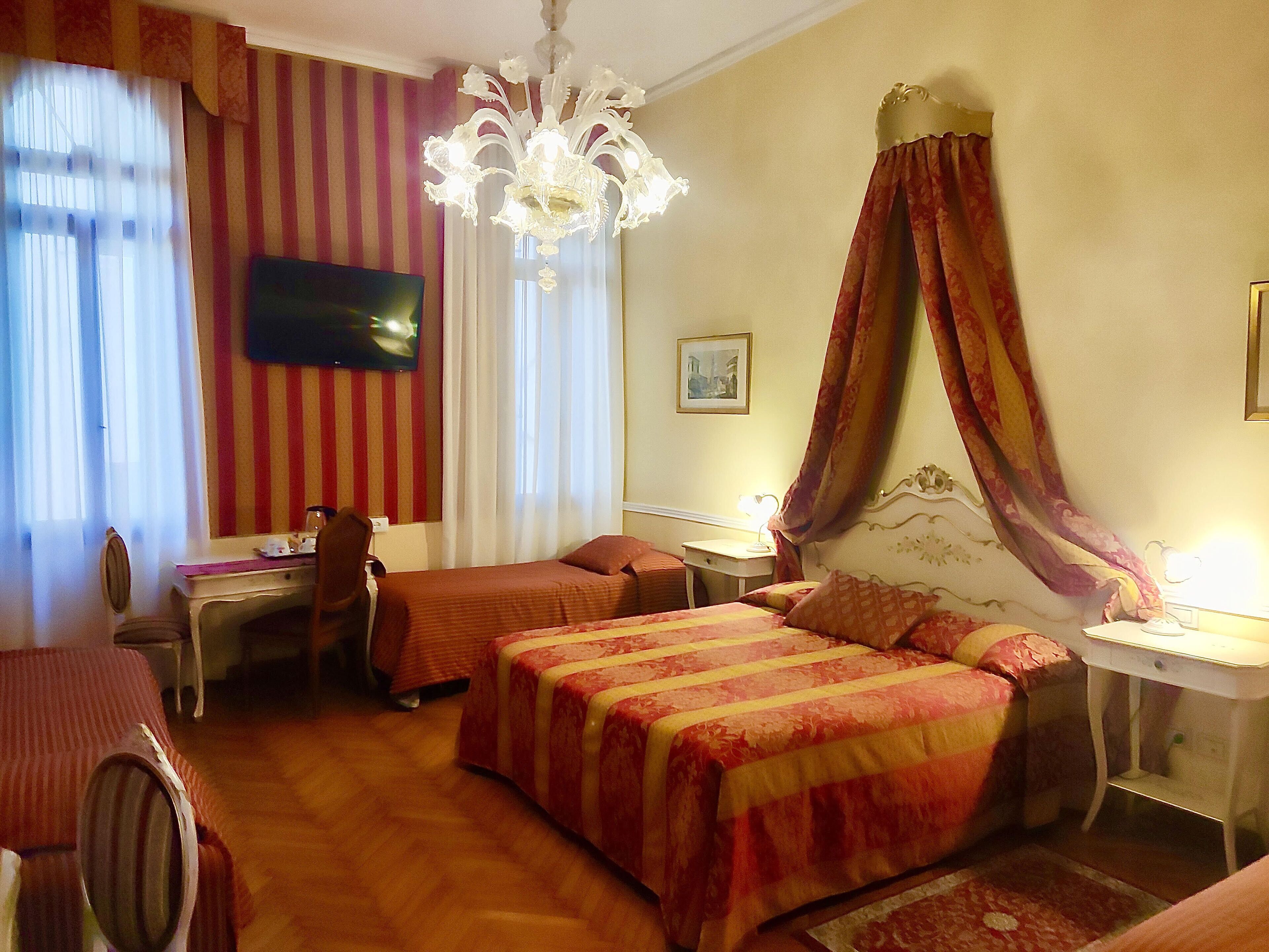 A hotel room with a bed, a desk, a chair, a television, and a chandelier.