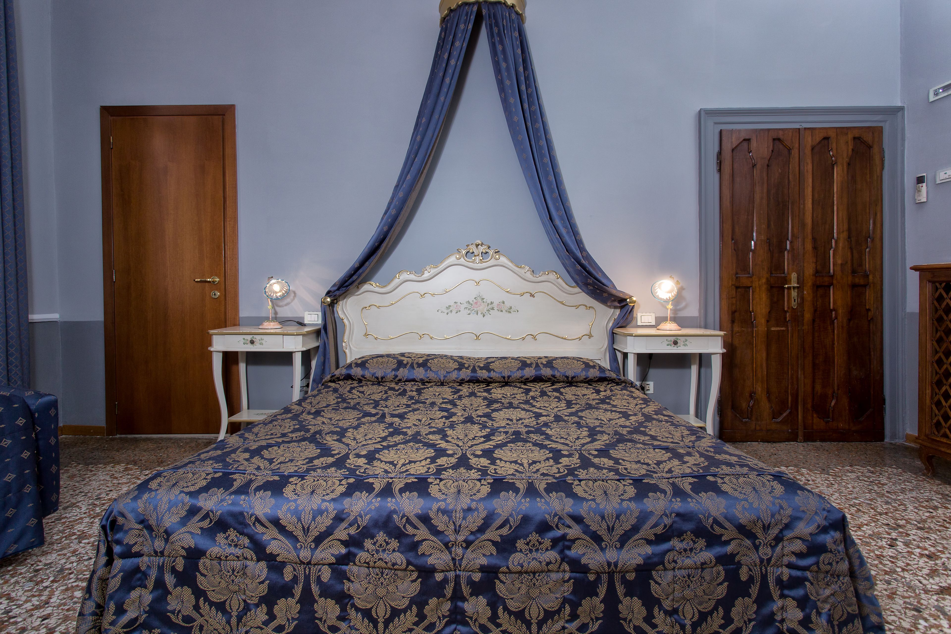 A bedroom with a large bed, two bedside tables, a wooden wardrobe, and a blue curtain over the bed.