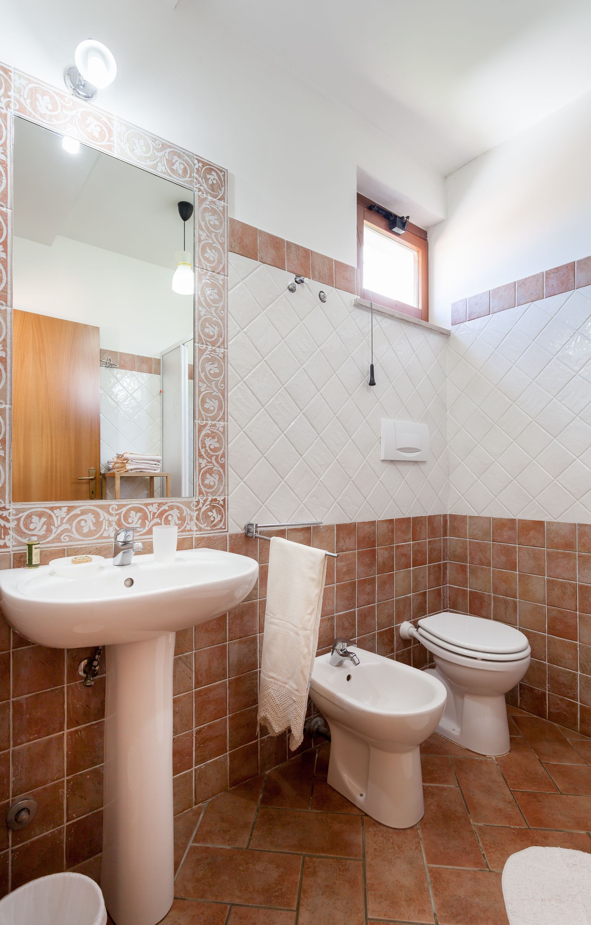 Un baño con lavamanos, bidé, inodoro, paredes revestidas de azulejos y un espejo con luz.