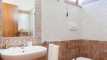 Un baño con lavamanos, bidé, inodoro, paredes revestidas de azulejos y un espejo con luz.