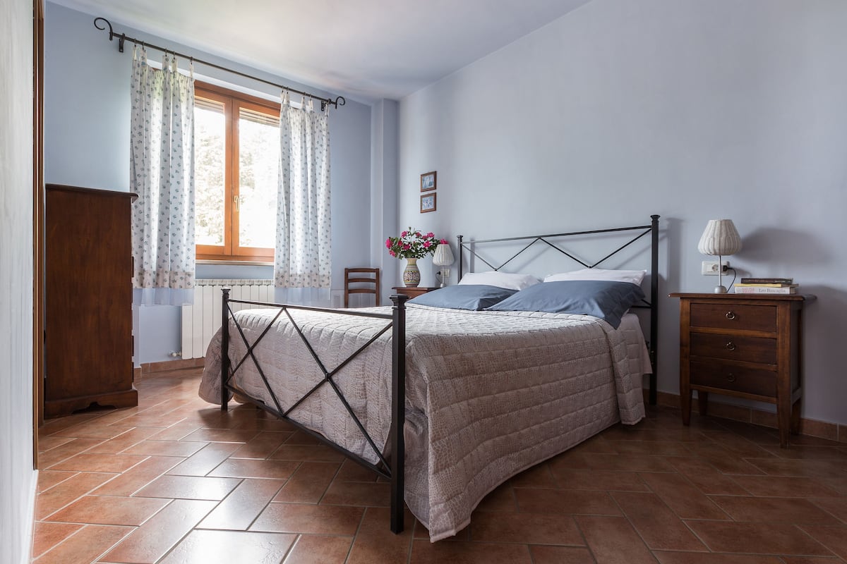 A bedroom with a bed, a nightstand, a dresser, and a window with curtains.