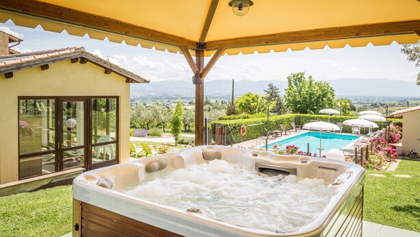 A hot tub under a yellow canopy with a view of a swimming pool and mountains.