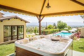 A hot tub under a yellow canopy with a view of a swimming pool and mountains. - Country House Nonna Rana (Cannara)