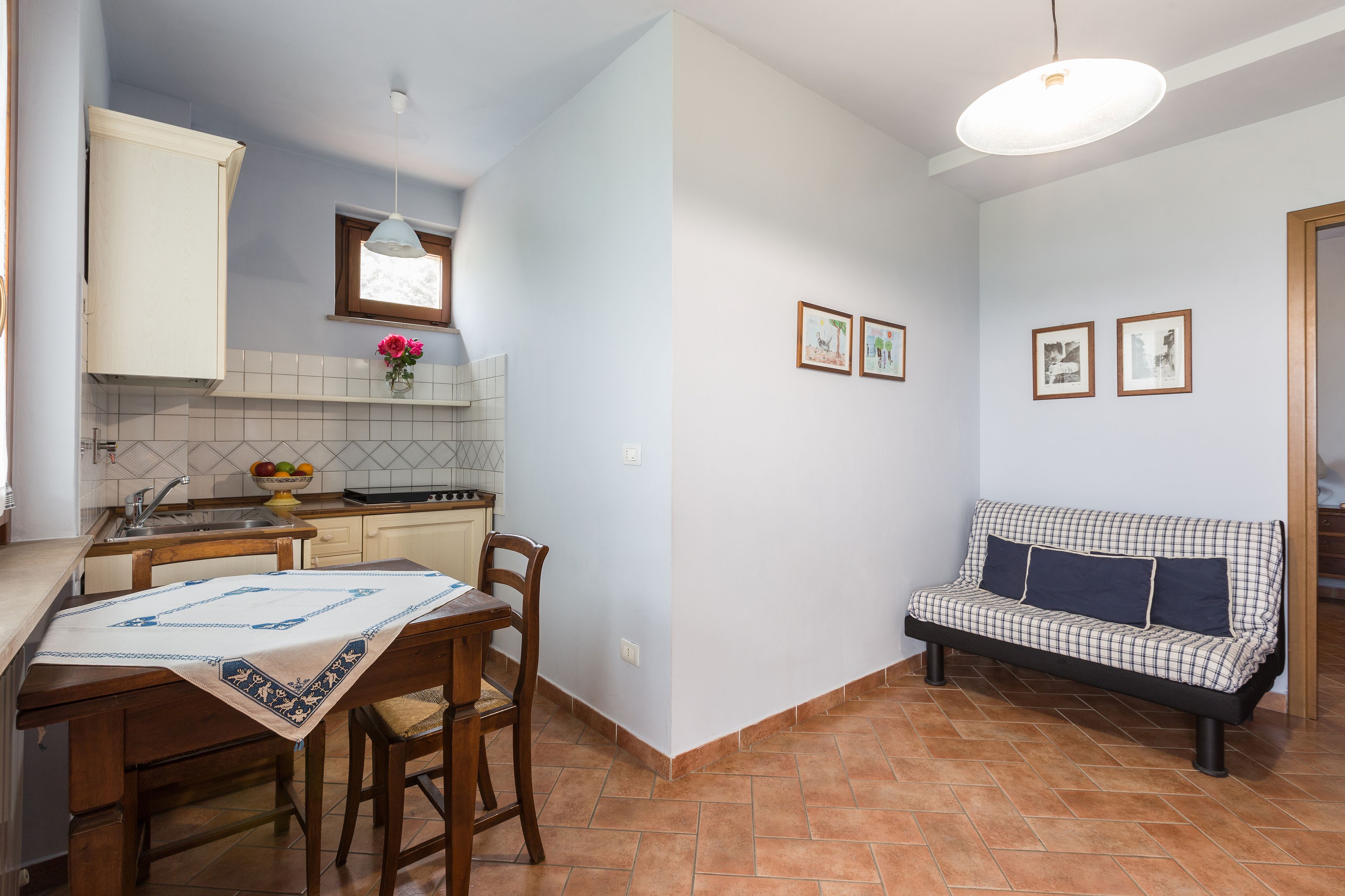 Una cocina compacta con una mesa de comedor, sillas, un sofá y una lámpara colgante.