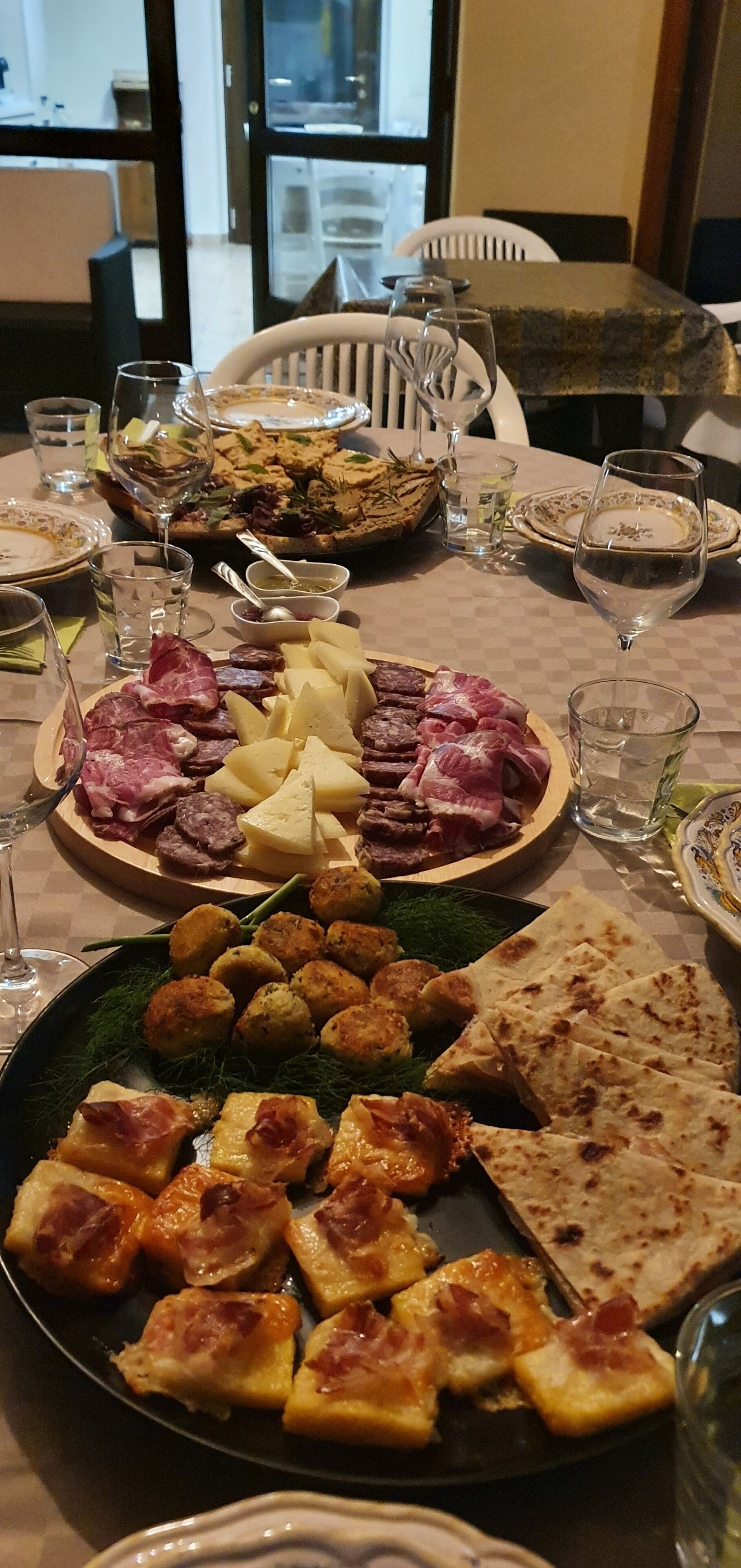 Una tavola imbandita con diversi piatti, tra cui carni, formaggi e focacce, insieme a bicchieri d'acqua e di vino.
