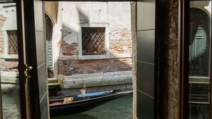 A narrow waterway with a gondola docked at a building with a brick facade and a window with a metal grille. - Locanda Leon Bianco on the Grand Canal (Venice)