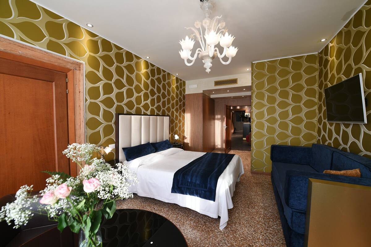 Quarto de hotel com cama, sofá, televisão e lustre.