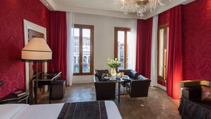 A hotel room with a bed, a desk, a chair, a table with a vase of flowers, and a chandelier. - Locanda Leon Bianco on the Grand Canal (Venice)