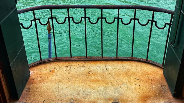 A balcony with a metal railing overlooking a canal with boats and a historic building in the background. - Locanda Leon Bianco on the Grand Canal (Venice)