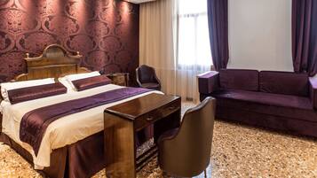 Ein Hotelzimmer mit Bett, Schreibtisch, Sessel, Sofa und einem großen Fenster mit Vorhängen.