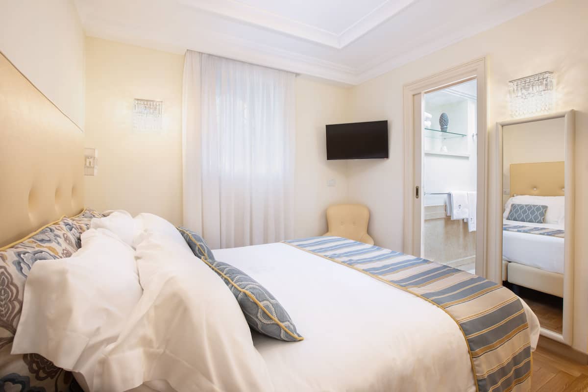 A hotel room with a bed, a television, a chair, and a bathroom visible through an open door.