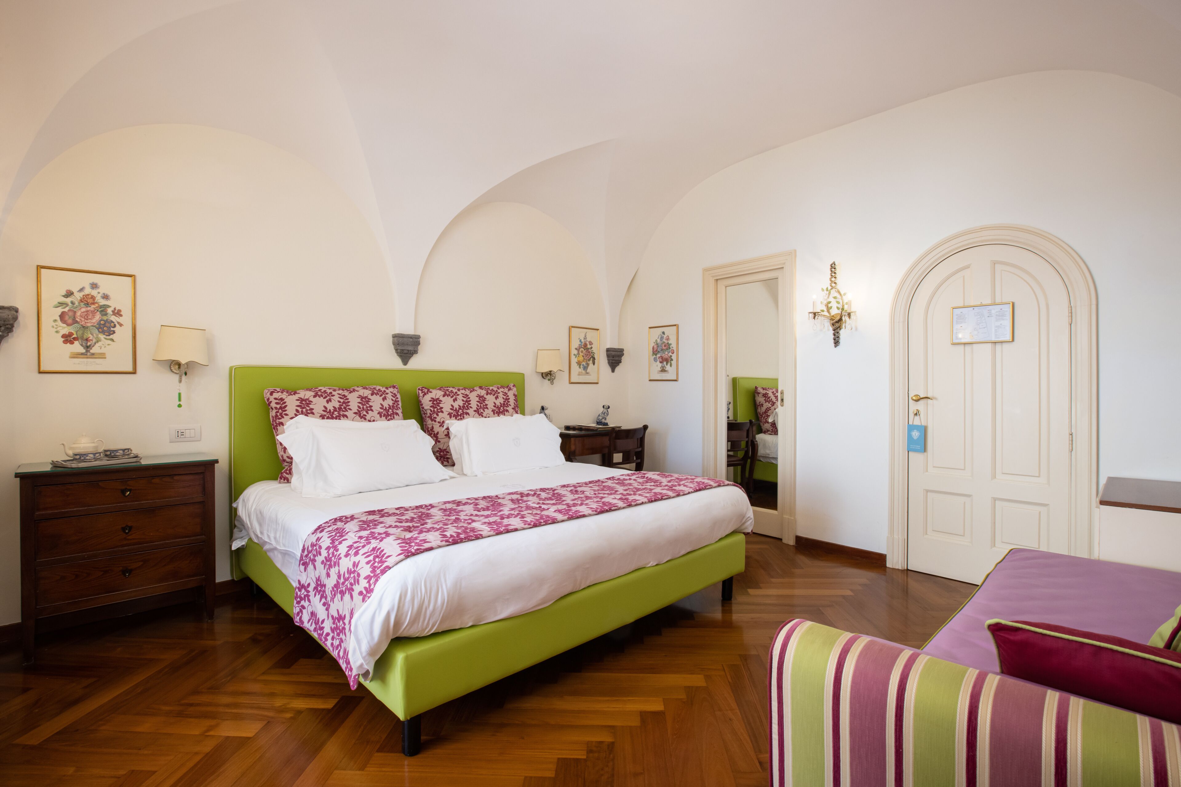 A bedroom with a green bed, white bedding, a wooden dresser, a nightstand, a chair, and a door with a sign.