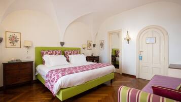 A bedroom with a green bed, white bedding, a wooden dresser, a nightstand, a chair, and a door with a sign.