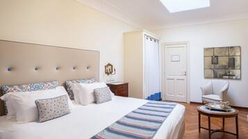 A hotel room with a large bed, a bedside table, a chair, a small table with a tray, and a painting on the wall.