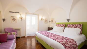 A bedroom with a green headboard, a large bed with floral bedding, a pink armchair, and a wooden floor.