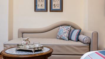 A beige sofa with patterned cushions, a small round table with a tray of silverware and a pitcher, and two framed sketches on the wall.