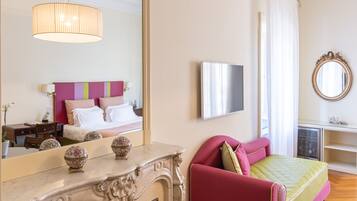Una habitación de hotel con cama, un sillón rojo, un espejo grande, televisor y chimenea.