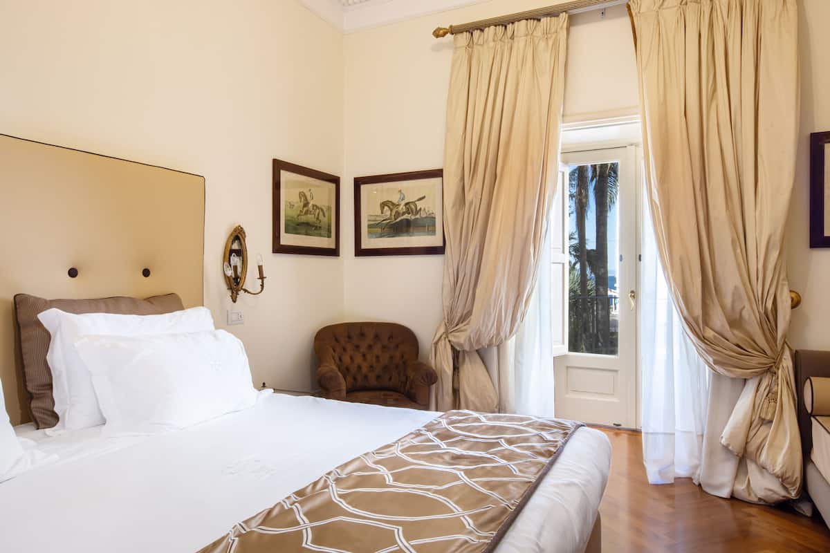 A hotel room with a bed, a chair, and two framed pictures on the wall.